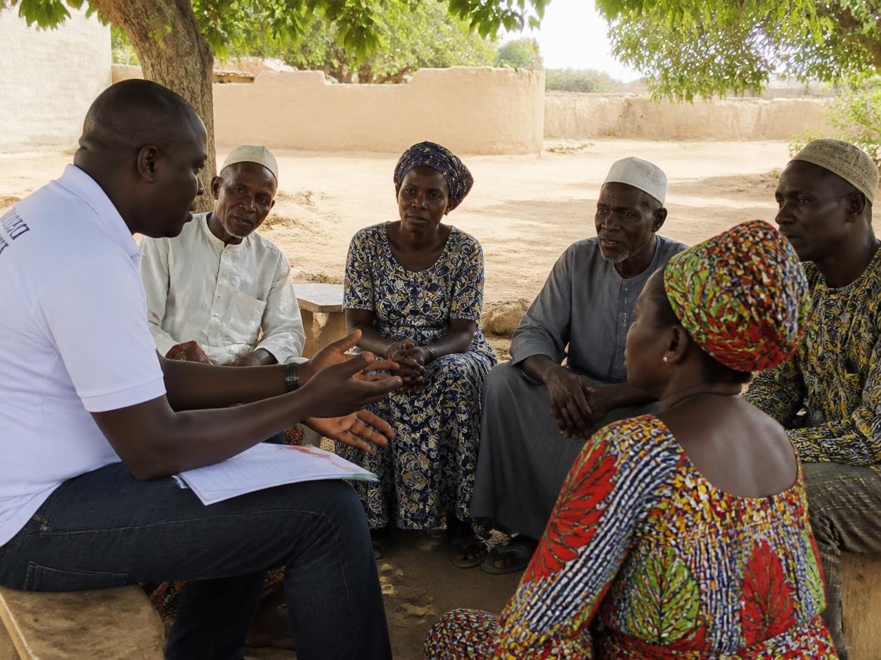 A programme facilitator in conversation with community members outdoors